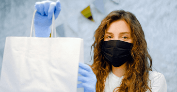 Woman holds shopping bag wearing gloves and mask